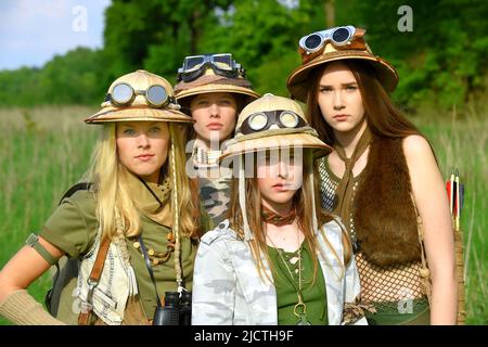 Quattro ragazze sono viste come esploratori. Sono visti al loro campeggio nella natura selvaggia all'aperto. Indossano cappelli safari e abiti cachi. Foto Stock