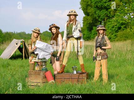 Quattro ragazze sono viste come esploratori. Sono visti al loro campeggio nella natura selvaggia all'aperto. Indossano cappelli safari e abiti cachi. Foto Stock