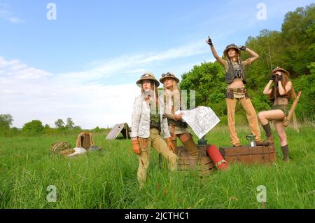 Quattro ragazze sono viste come esploratori. Sono visti al loro campeggio nella natura selvaggia all'aperto. Indossano cappelli safari e abiti cachi. Foto Stock