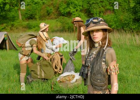 Quattro ragazze sono viste come esploratori. Sono visti al loro campeggio nella natura selvaggia all'aperto. Indossano cappelli safari e abiti cachi. Foto Stock