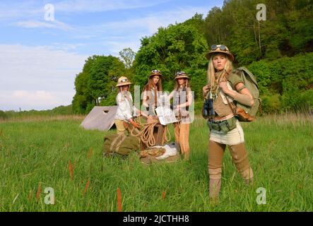 Quattro ragazze sono viste come explorers.They installare un campeggio nella natura selvaggia esterna. Indossano cappelli safari e abiti cachi. Foto Stock