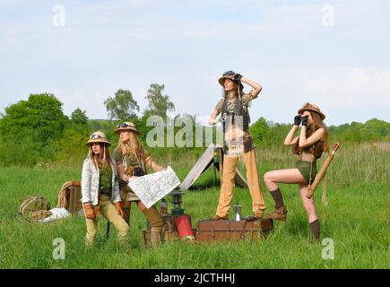 Quattro ragazze sono viste come explorers.They installare un campeggio nella natura selvaggia esterna. Indossano cappelli safari e abiti cachi. Foto Stock