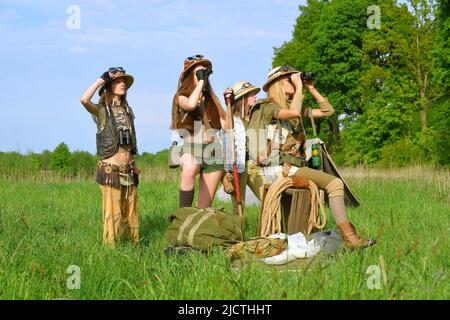 Quattro ragazze sono viste come explorers.They installare un campeggio nella natura selvaggia esterna. Indossano cappelli safari e abiti cachi. Foto Stock