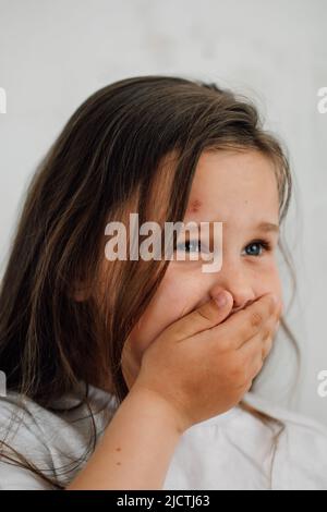 ritratto di piccola ragazza triste livida con capelli lunghi e scuri che ricoprono la bocca con la mano. Protesta contro gli abusi. Foto Stock