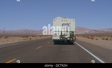 Nevada: Parte posteriore di un camper con due biciclette su un portabiciclette mostrato guidare su un'autostrada solitaria nel deserto in una giornata di sole. Foto Stock