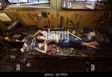 Una giovane bella donna trova il tempo di dormire durante le sue ore lavorative. Si trova sul banco di lavoro pieno di strumenti e altri dispositivi elettronici. Foto Stock