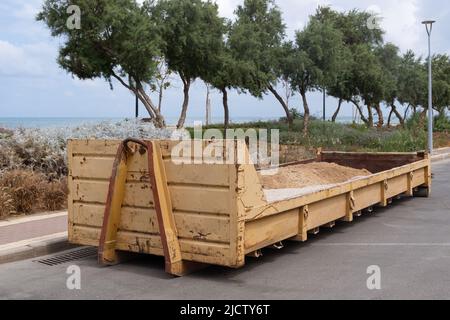 Contenitore del serbatoio dei rifiuti in metallo della spazzatura riempito di terreno e macerie vicino a un cantiere. Foto Stock