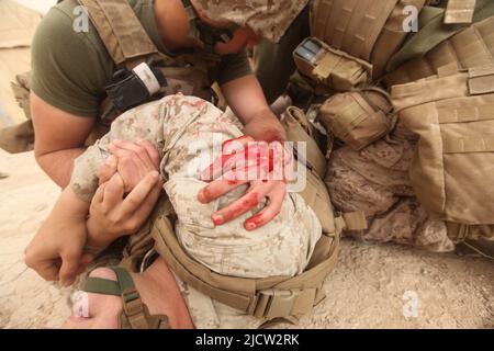 I Marines E il Corpsman della Marina DEGLI STATI UNITI amministrano il primo aiuto ad un colpo della pistola ha ferito la Marina durante un fuoco a Kajaki, Afghanistan. Foto Stock