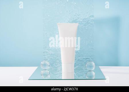 Mockup tubo in plastica bianca crema cosmetica senza marchio su sfondo blu con eleganti puntine, specchio e sfere di vetro, piastra acrilica. Corpo e assistenza sanitaria Foto Stock