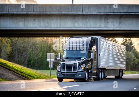 Semirimorchio industriale nero lucido a lunga percorrenza con cofano da braccio grande trattore per il trasporto di carichi commerciali in semirimorchio refrigerato di dimensioni normali che gira su Foto Stock