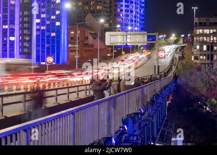 Con edifici illuminati dietro di loro e proiettori di luce montati sotto, fotografi con telecamere, cavalletti e telefoni si allineano lungo la Cahill Expressway Foto Stock