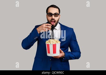 L'uomo impressionato che ottiene l'esperienza VR visore, usando la realtà aumentata occhi essere in realtà virtuale, guardare film con popcorn. Studio interno girato isolato su sfondo grigio. Foto Stock