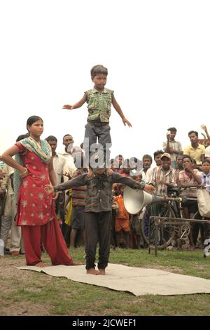 I bambini che effettuano una stunt di ginnastica davanti a decine di spettatori su un campo stradale alla periferia di Rajgir in Bihar, India. Foto Stock