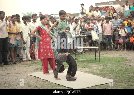 I bambini che effettuano una stunt di ginnastica davanti a decine di spettatori su un campo stradale alla periferia di Rajgir in Bihar, India. Foto Stock