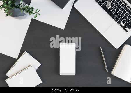 Vista dall'alto su uno schermo bianco bianco e moderno per smartphone con notebook, notebook, uomini e carte su un tavolo nero. 3D rendering, mockup Foto Stock