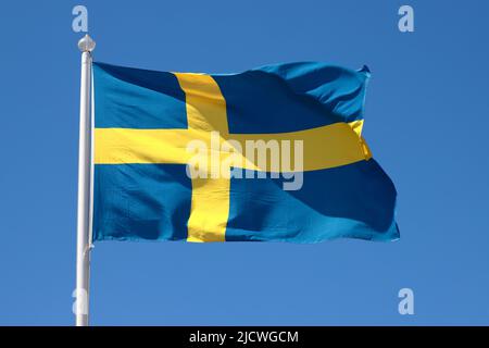 Vista ravvicinata di una bandiera svedese issata contro un cielo blu chiaro. Foto Stock