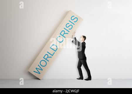 Concetto di crisi mondiale con uomo in abito nero cercando di spingere pesante segno di legno con le parole di crisi mondiale su sfondo chiaro astratto Foto Stock