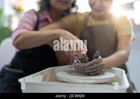 Laboratorio di ceramica. Senior insegna ceramica giovane donna asiatica. Modellazione di argilla Foto Stock