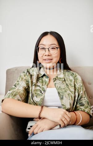 Ritratto minimo di ragazza adolescente asiatica con bretelle sorridenti alla macchina fotografica mentre si siede in poltrona Foto Stock