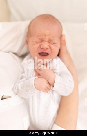 Madre irriconoscibile che tiene il suo figlio neonato piangere a casa, primo piano Foto Stock