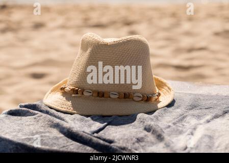 Cappello di paglia adornato con guscio, posto su un telo da spiaggia. Estate calda. Protezione della testa. Vacanze, sole, spiaggia e relax. Posiziona per testo Foto Stock