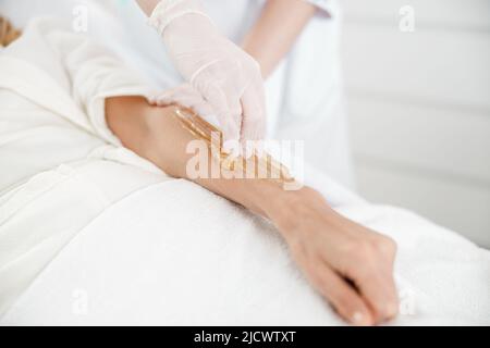 Il professionista sta facendo depilazione zuccherante dei capelli sulla mano femminile nel centro di cosmetologia Foto Stock