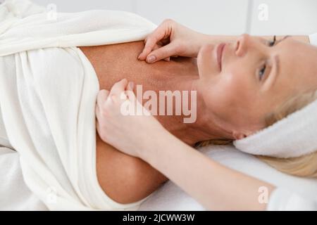 Felice cliente sicuro femmina ottenere massaggio nel gabinetto cosmetologist, procedura di spa Foto Stock