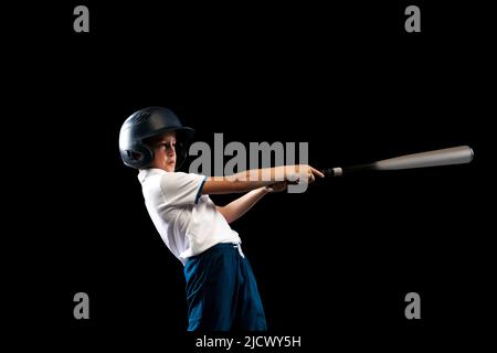 Scatto dello studio del capretto sportivo, giocatore di baseball principiante in uniforme di sport che gioca il baseball isolato su sfondo nero. Concetto di sport, realizzazioni Foto Stock