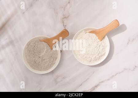 Vista dall'alto su due ciotole bianche con argilla cosmetica grigia e bianca su tavolo di marmo bianco - polvere minerale, maschera facciale bentonite. Concetto di bellezza per la cura della pelle. Foto Stock