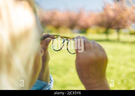 Vista scarsa, mano che tiene eleganti occhiali da cornice su uno sfondo verde sfocato Foto Stock