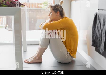 donna solitario depressa e malata seduta da sola sul piano della cucina in stress , depressione e tristezza sensazione di miserabile a piedi nudi cercando disperato Foto Stock