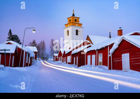 I percorsi automobilistici si illuminano sulla strada ghiacciata che attraversa la medievale città della chiesa di Gammelstad coperta di neve, patrimonio dell'umanità dell'UNESCO, Lulea, Svezia Foto Stock