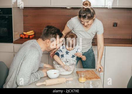 Giovane carina famiglia di madre, padre, figlio che cottura biscotti in cucina a casa, ragazzo 4 anni indipendentemente impasta pasta, è appassionato di processo, felice Foto Stock