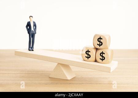 Concetto di equilibrio tra vita e lavoro o denaro. Figurine uomo d'affari e simbolo del dollaro su blocchi di legno su seesaw di legno Foto Stock