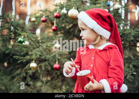 Natale nel mese di luglio. Bambino in attesa di Natale in legno nel mese di luglio. Ritratto di bambina che beve cioccolata calda con marshmallow e zenzero uomo biscotti. Buon Natale e buone feste. Foto Stock