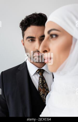 Uomo musulmano che guarda la sposa sfocata in primo piano isolato su grigio Foto Stock