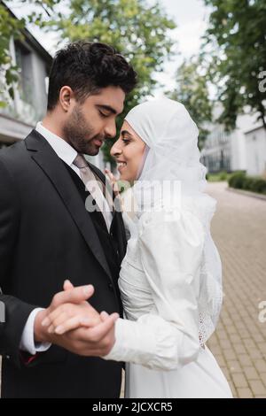 felice sposa musulmana e sposo con occhi chiusi che tengono le mani Foto Stock