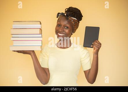 giovane donna che confronta i libri stampati con l'e-book mentre trasporta i libri sulla sua mano destra e un ebook sulla sua mano sinistra guardando la macchina fotografica Foto Stock