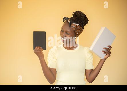 giovane donna che confronta i libri stampati con l'e-book mentre tiene un libro sulla sua mano sinistra mentre smacling all'e-book sulla sua mano destra Foto Stock