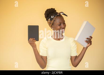 giovane donna che confronta i libri stampati con e-book mentre un e-book sulla sua mano destra mentre smacling a libro stampato sulla sua mano sinistra Foto Stock