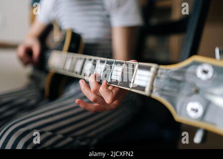 Primo piano ripresa ritagliata di una ragazza preteen irriconoscibile imparare a suonare la chitarra usando la chitarra elettrica per la musica auto studio a casa, fuoco selettivo. Foto Stock