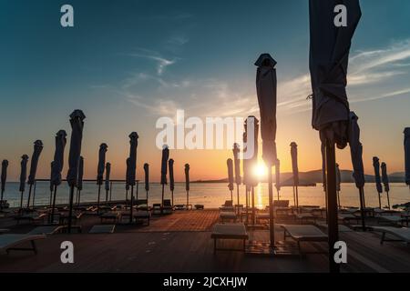 Tramonto sulla spiaggia del resort con lettini e ombrelloni arrotolati. Foto Stock