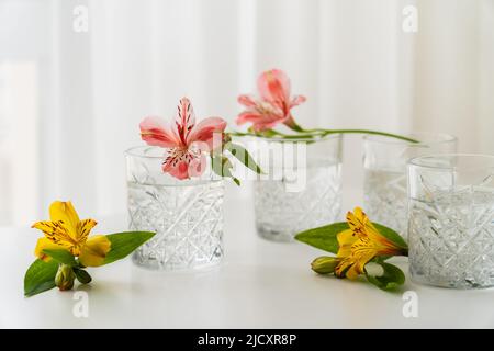 fiori di alstroemeria gialli e rosa vicino a bicchieri con acqua sul piano portapaziente bianco Foto Stock