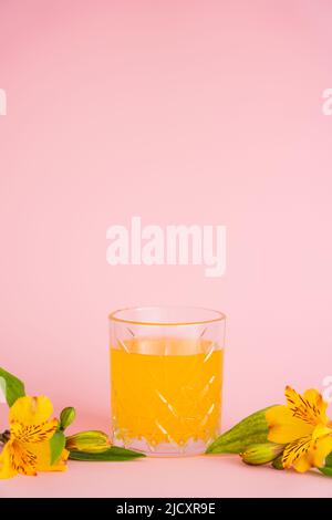 bicchiere di succo fresco di agrumi e fiori tropicali gialli su sfondo rosa Foto Stock