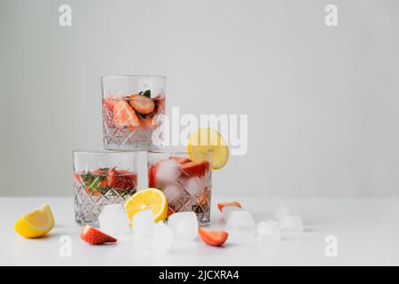 bevanda tonica rinfrescante con fragole vicino ai limoni tagliati e cubetti di ghiaccio isolati sul grigio Foto Stock