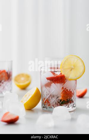 fuoco selettivo di acqua tonica con fragole e ghiaccio vicino ai limoni tagliati su sfondo bianco sfocato Foto Stock