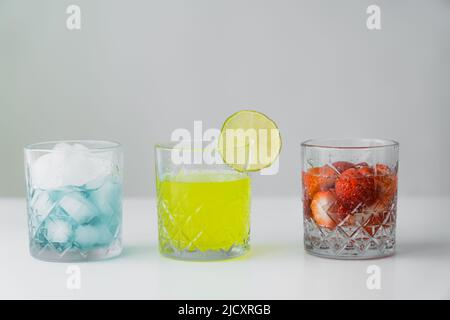 limonata e fragola tonico vicino al bicchiere con cubetti di ghiaccio su superficie bianca isolato su grigio Foto Stock