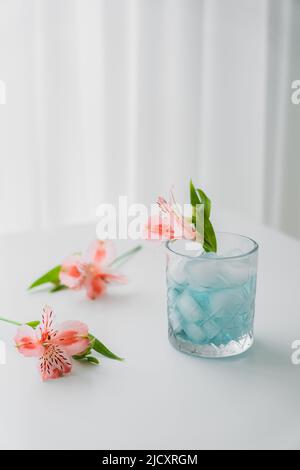 vetro con tonico freddo e fiore di alstroemeria rosa su piano portapaziente bianco e sfondo grigio Foto Stock