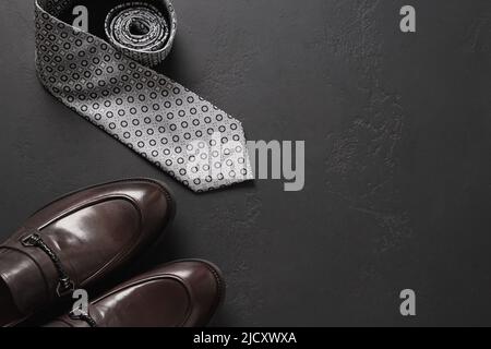 Set di accessori da uomo - scarpe marroni, cravatta su sfondo nero. Vista dall'alto. Spazio di copia. Felice Giornata dei Padri. Foto Stock