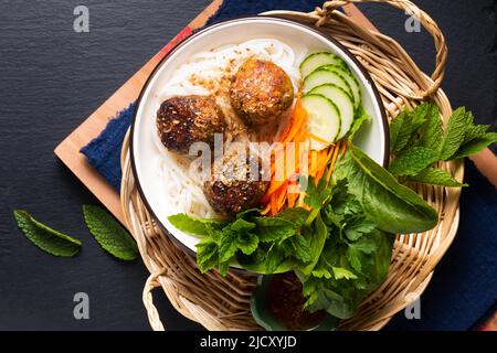 Concetto di cibo Bun Cha spaghetti di riso vietnamiti e polpette di carne con verdure ed erbe su sfondo nero con spazio copia Foto Stock